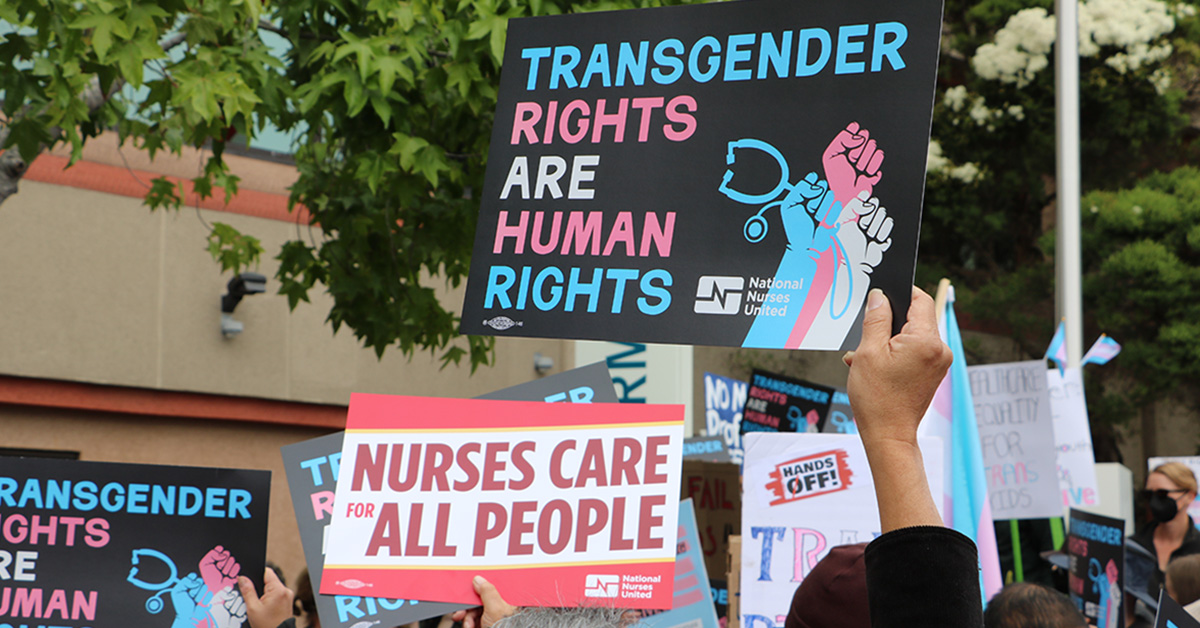 Hands holding signs "Transgender Rights Are Human Rights" and "Nurses Care for All People"