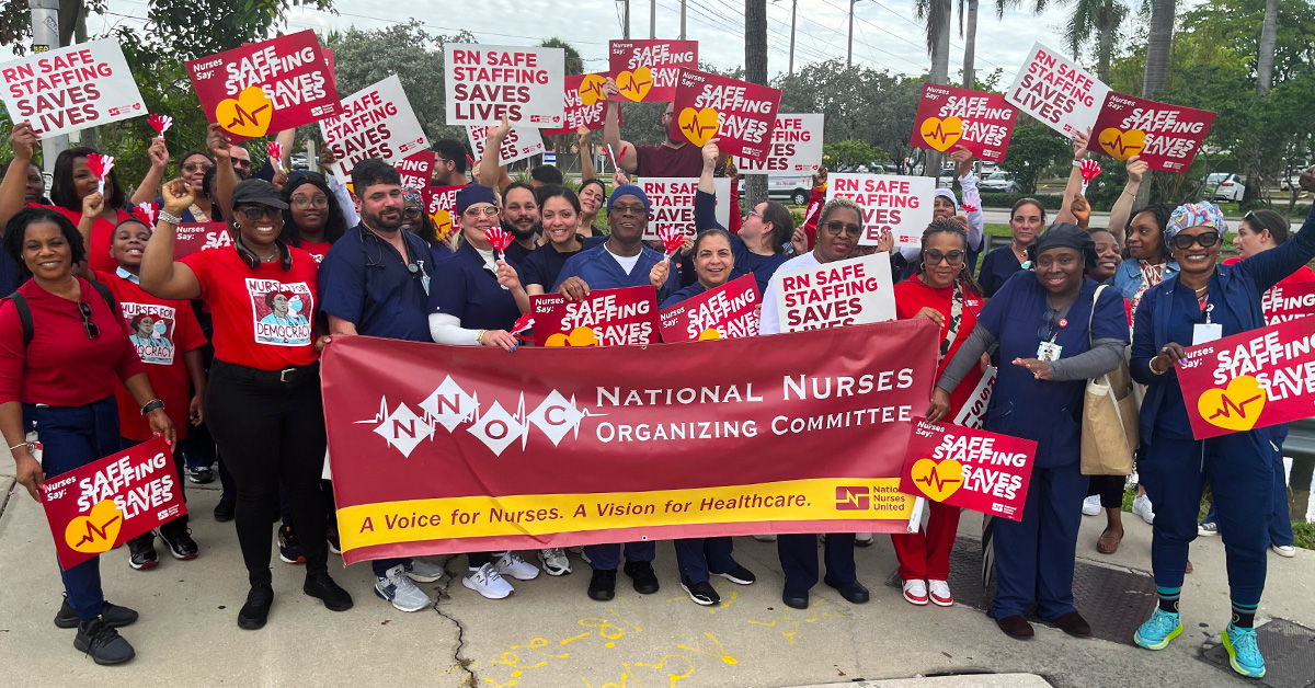 Large group of nurses outside, holding signs calling for safe staffing and NNOC banner