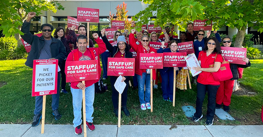 Large group of nurses outside hospital holding signs "Staff Up for Safe Patient Care"
