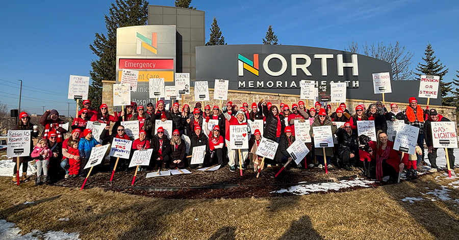 Large group of nurses outside of hospital holding picket signs 