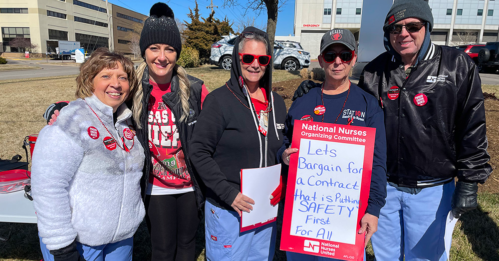 Five nurses outside hospital. One holds sign "Let's bargain for a contract that is putting SAFETY FIRST for all"