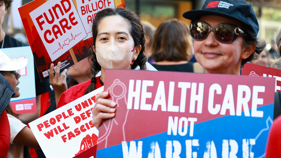 Nurse in march holding sign "Health Care Not Warefare"