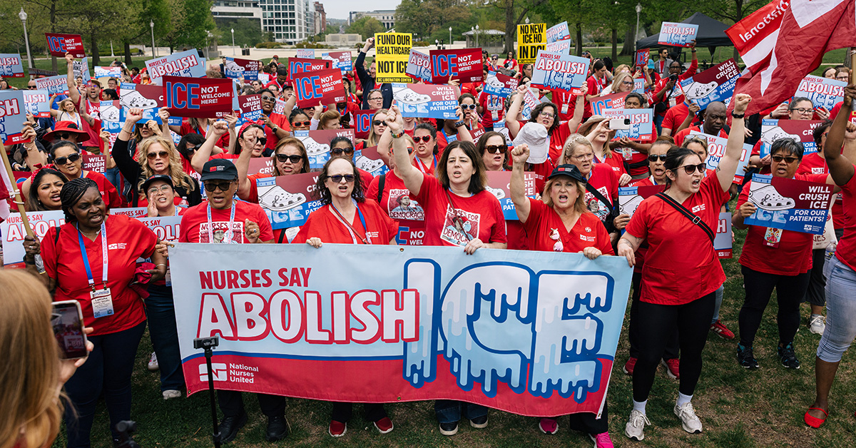 Large group of nurses outside, holding banner "Nurses Say Abolish ICE"