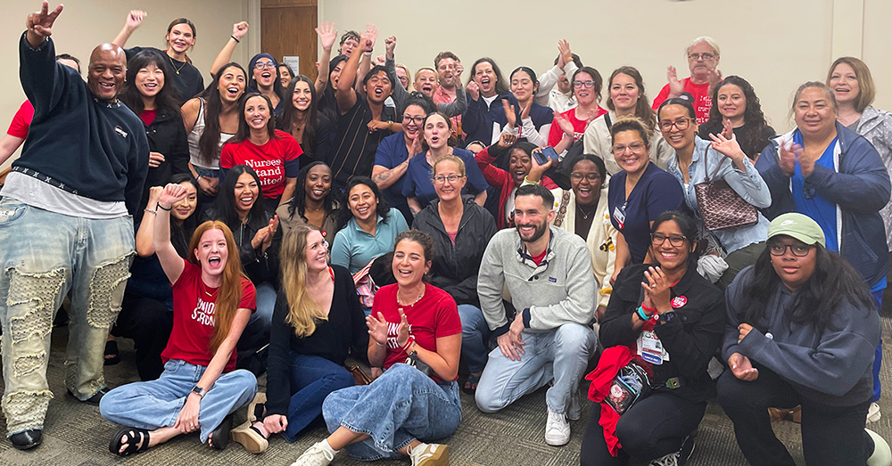 Large group of nurses inside hospital meeting room smiling with raised fists