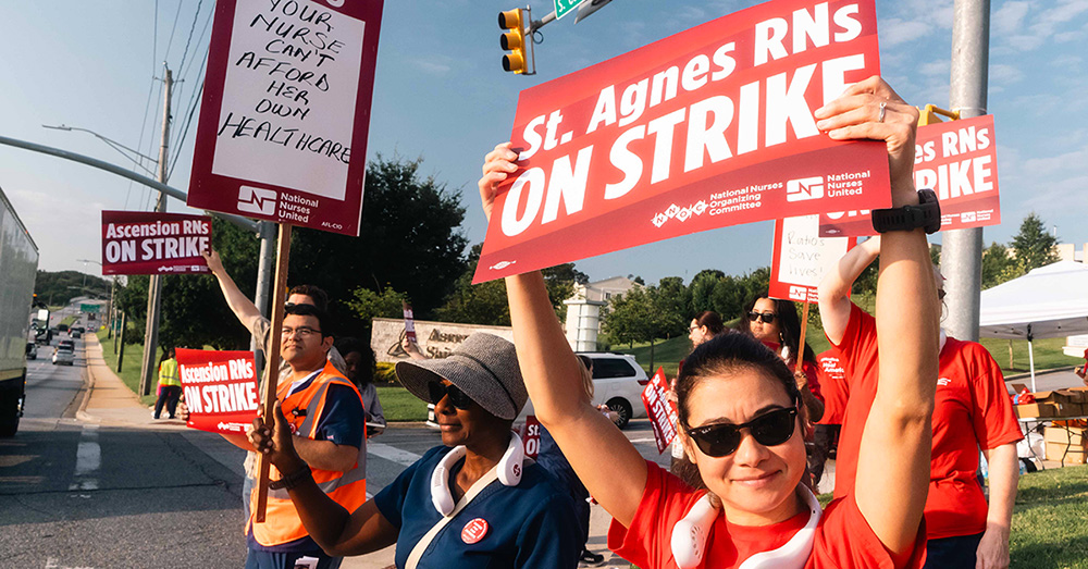 Nurse outside hospital holding sign "St. Agnes RNs ON STRIKE"
