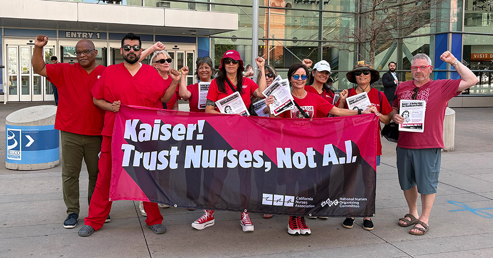 Group of nurses outside, with raised fists, holding banner "Kaiser! Trust Nurses Not A.I."