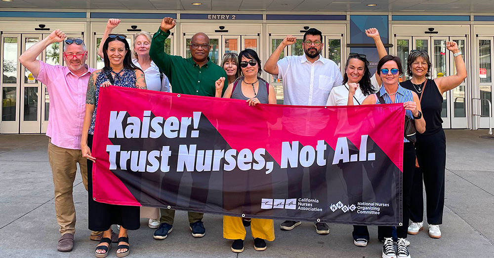 Group of nurses outside, with raised fists, holding banner "Kaiser! Trust Nurses, Not A.I."