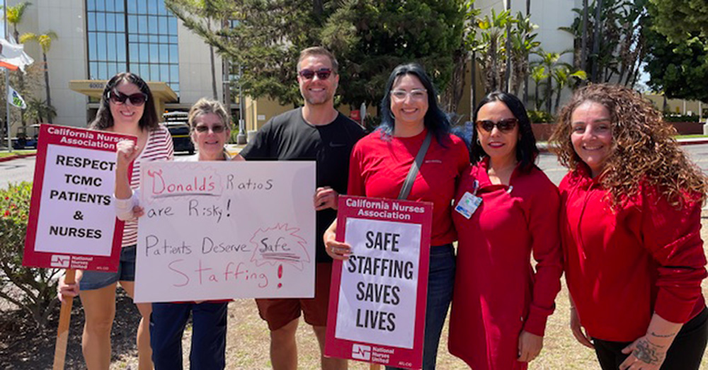 Six nurses standing outside hospital smiling, holding signs "Safe Staffing Saves Lives" and "Respect TCMC Patients and Nurses"