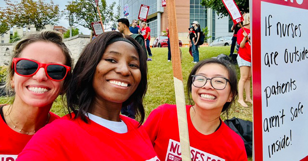 3 nurses outside hospital smiling, wearing red