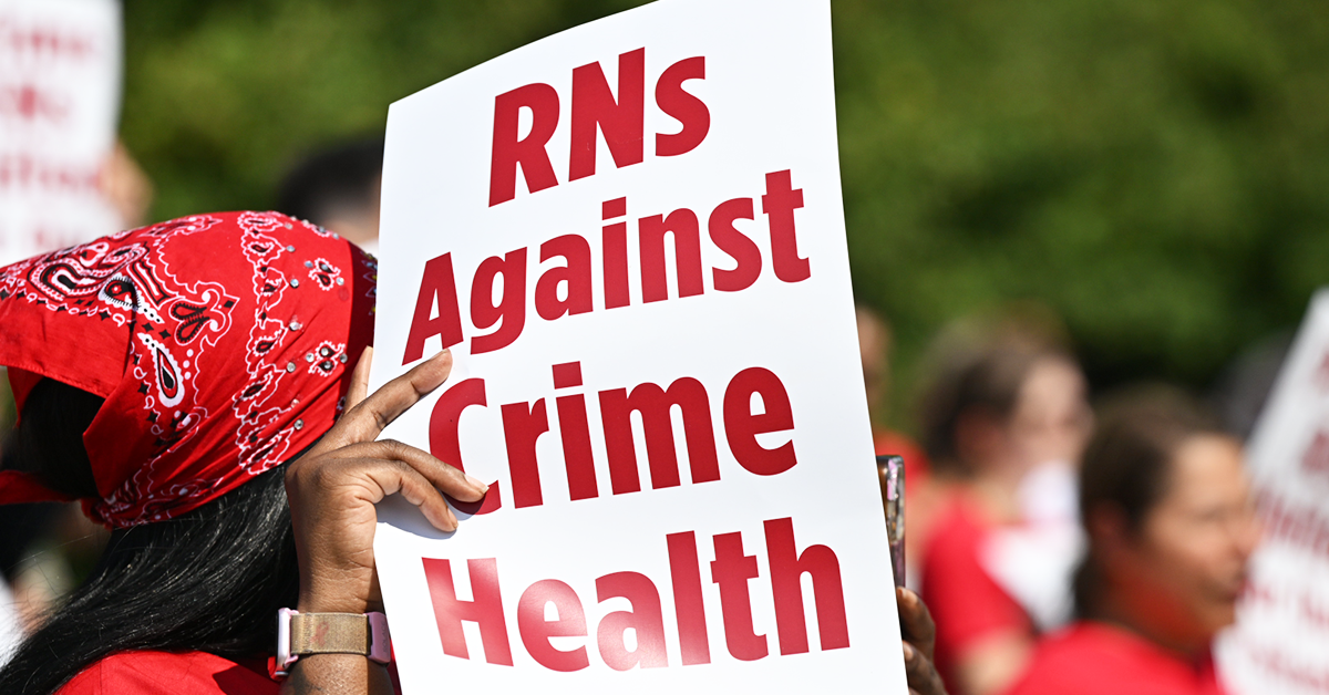 Nurse holding/shading herself with sign "RNs Against Crime Health"
