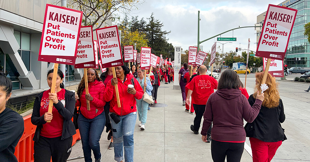 Nurses on picket line outside of hospital, holding signs "Kaiser: Put Patients Over Profits"