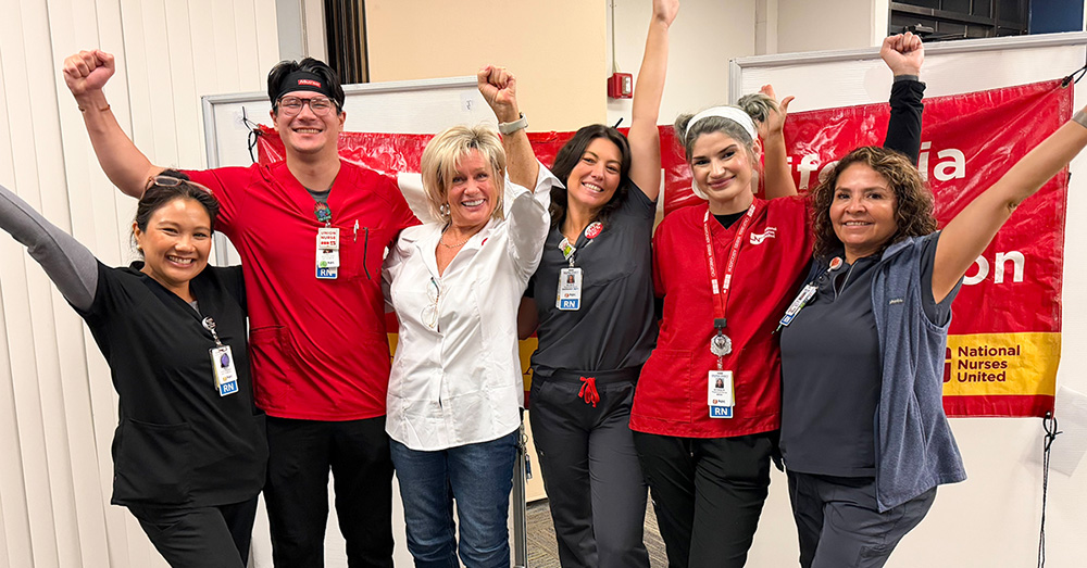 Six nurses inside, side-by-side, smiling, with raised arms/fists