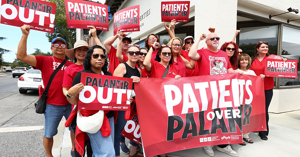Group of nurses hold signs and banner "Palantir Out" and "Patients Over Palantir"
