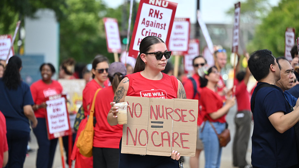 Nurse on picket line holds signs "No Nurses = No Care"