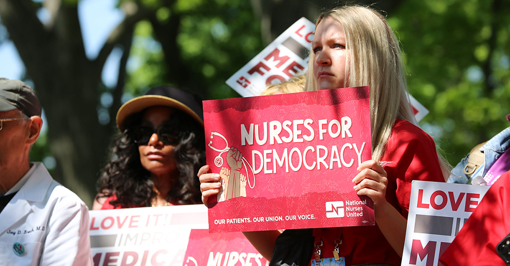 Nurse outside, holding sign "Nurses for Democracy"
