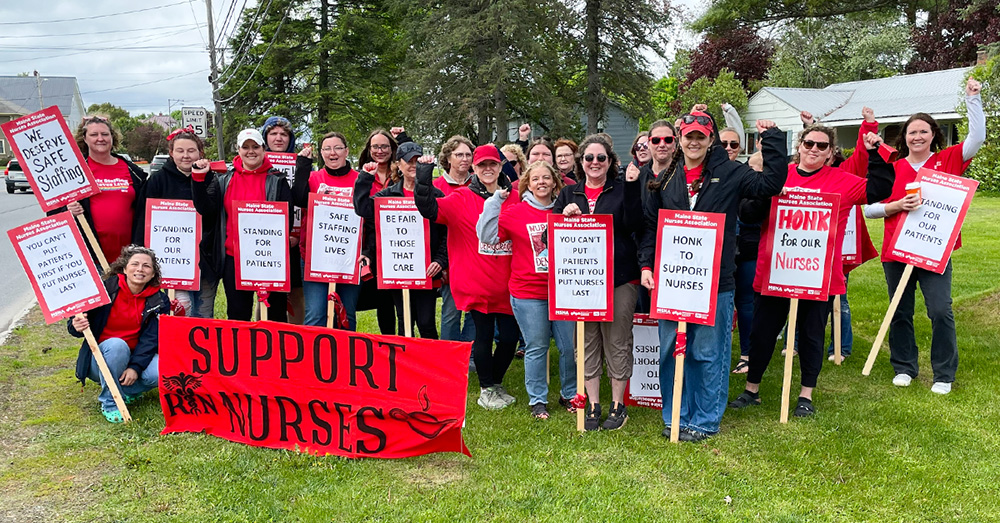 Large group of nurses outside, smiling, with raised fists, holding signs and banner "Support Nurses"