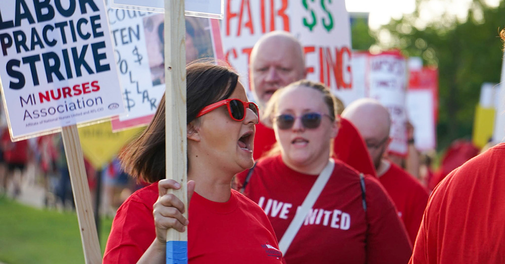 Nurse on strike line, one holds sign "Unfair Labor Practice Strike"