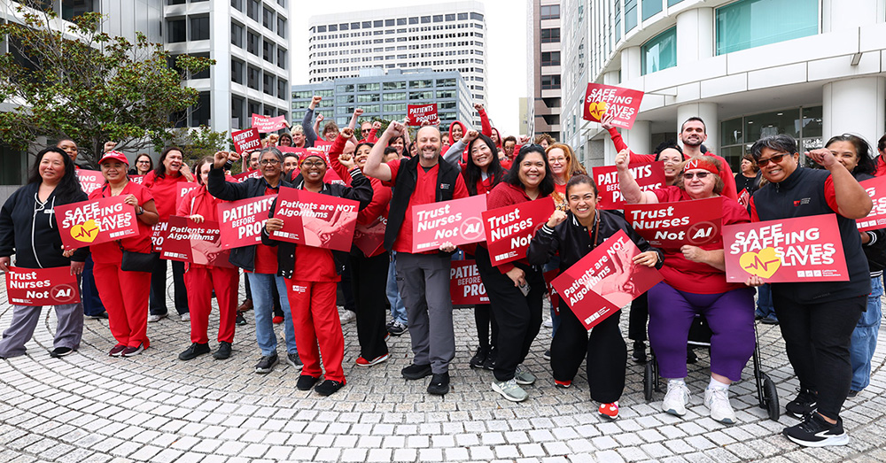 Large group of nurses rallying, holding signs "Safe Staffing Saves Lives", "Trust Nurses Not A.I."