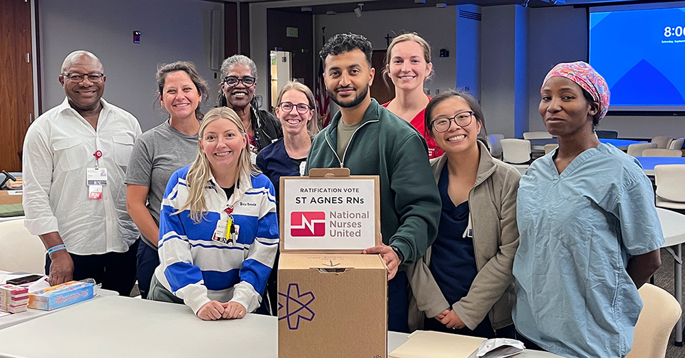 Group of nurses in conference room, behind ballot box, smiling