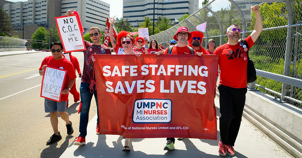 Nurses marching with raised fists, holding banner "Safe Staffing Saves Lives: UMPNC MI Nurses Association"