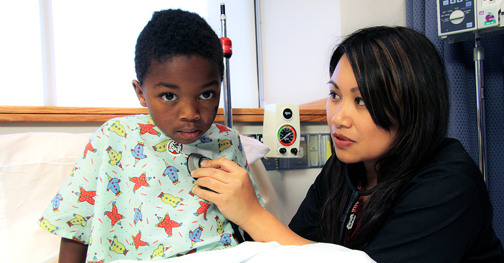 Nurse using stethoscope on child in hospital bed 