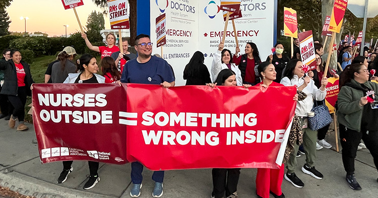 Nurses outside hospital holding banner "Nurses Outside = Something Wrong Inside"