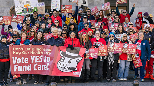 Large group of people behind banner "Vote YES to Fund Care!"