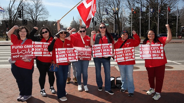 Nurses holding signs "Some Cuts Don't Heal" and "Fund Care Not Billionaires"