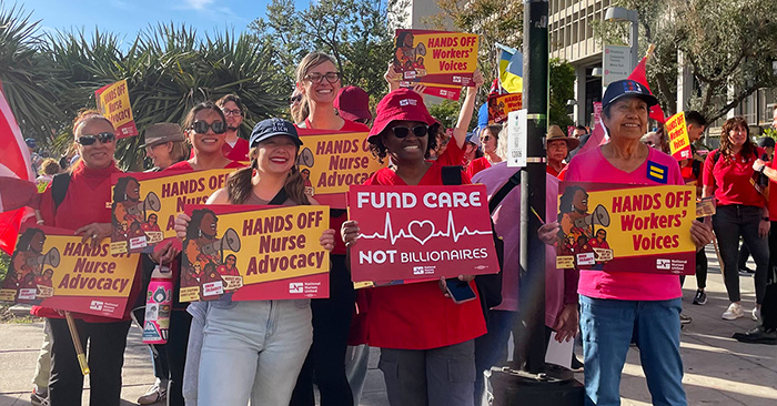 Nurses outside holding signs "Hands Off Workers Voices"