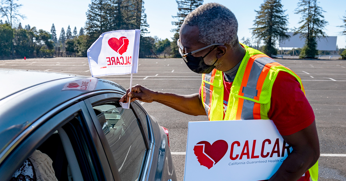 Person holding heart CalCare sign and placing flag on car.