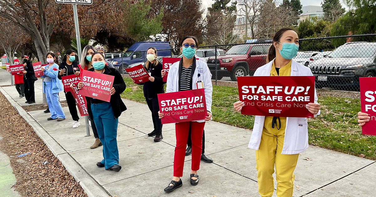 Group of four nurses outside hold signs "Staff up for safe patient care"