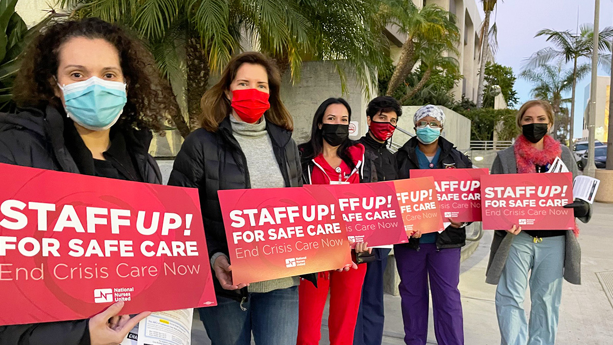 Group of nurses outside hospital hold signs "Staff Up for Safe Care"