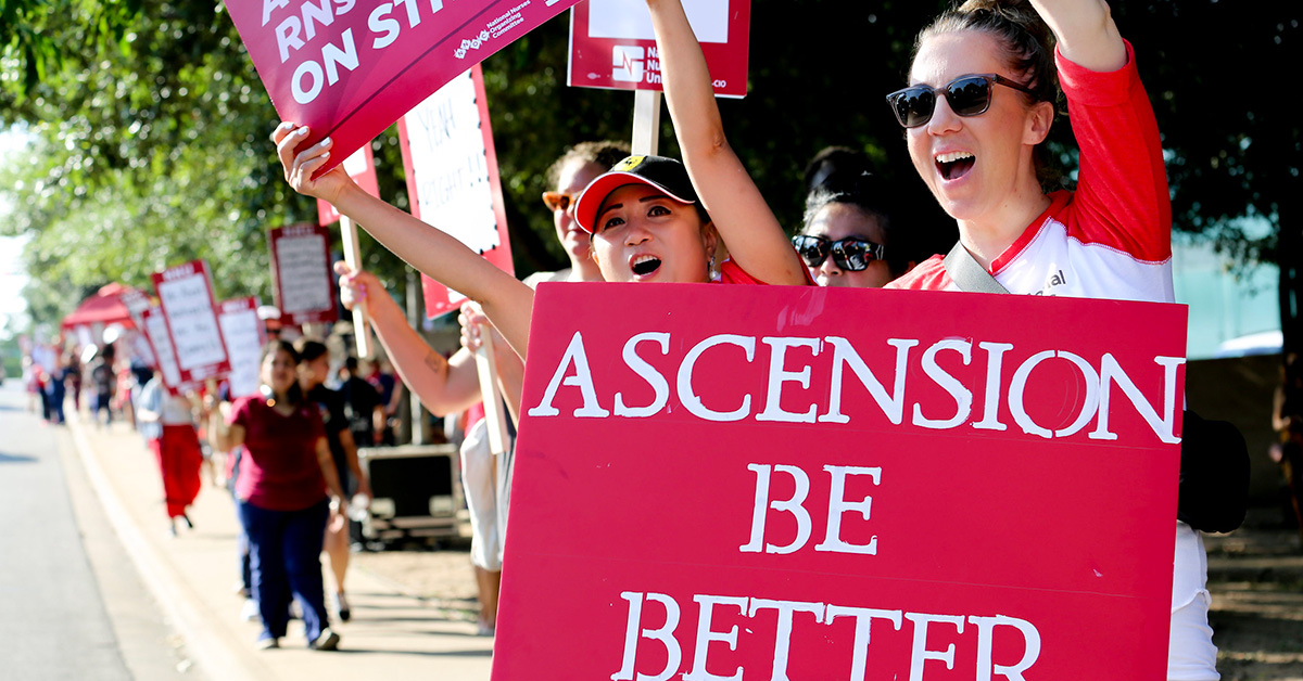 Nurse on picket line holds sign "Ascension Be Better"