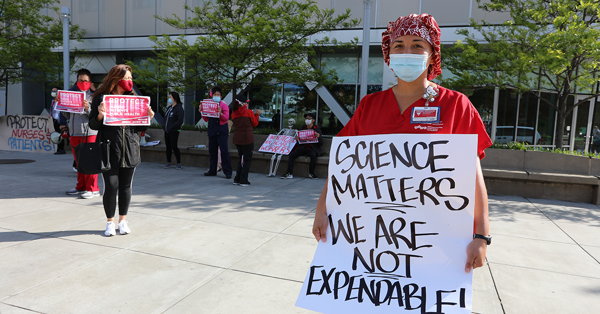Nurses outside with sign "Science matters we are not expendable" and "Protect nurses patients public health"