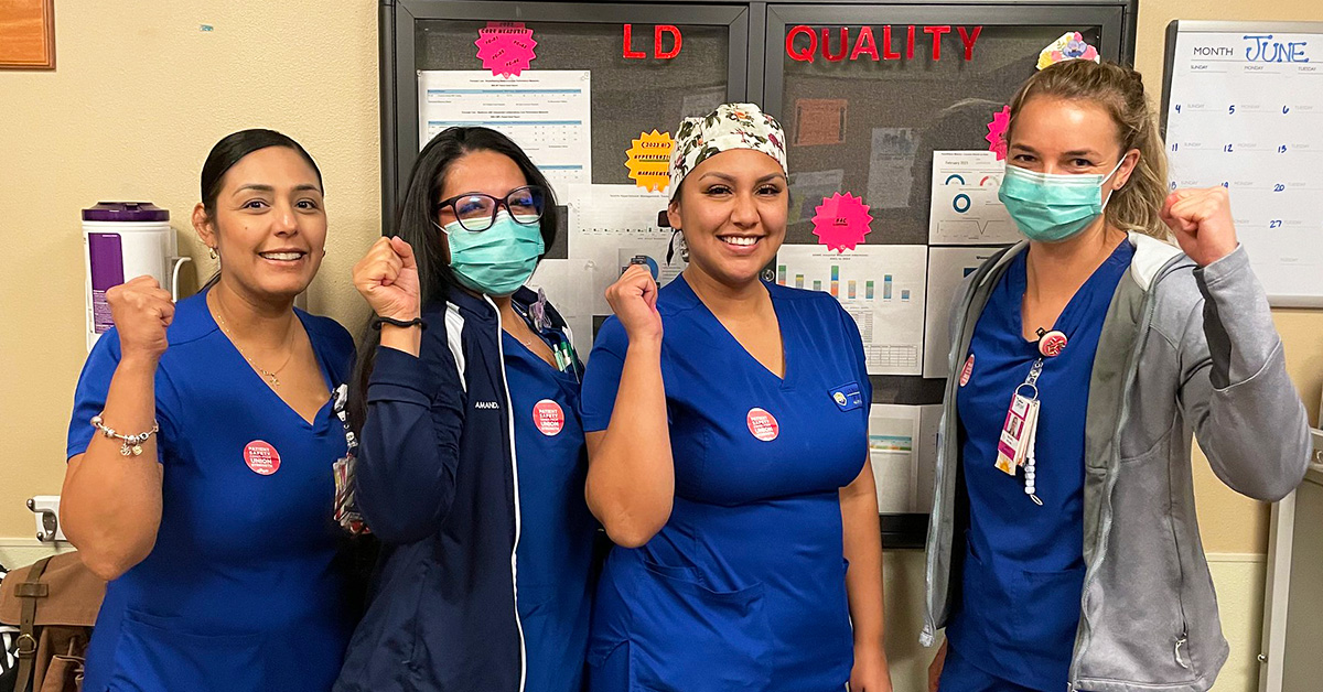 Four nurses inside hospital smiling and holding raised fists