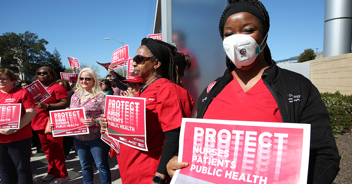 Nurses outside holding signs "Protect Nurses, Patients, Public Health"