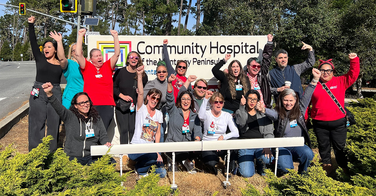 Group of nurses in front of hospital smiling, with raised fists