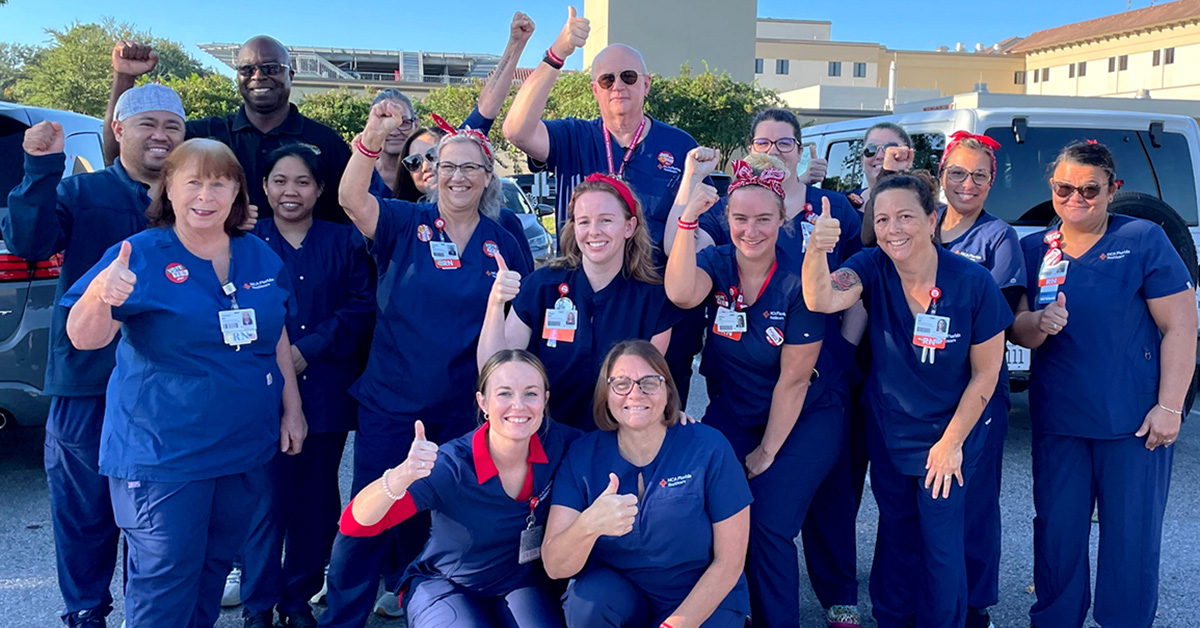 Large group of nurses outside hospital, smiling, with raised fists