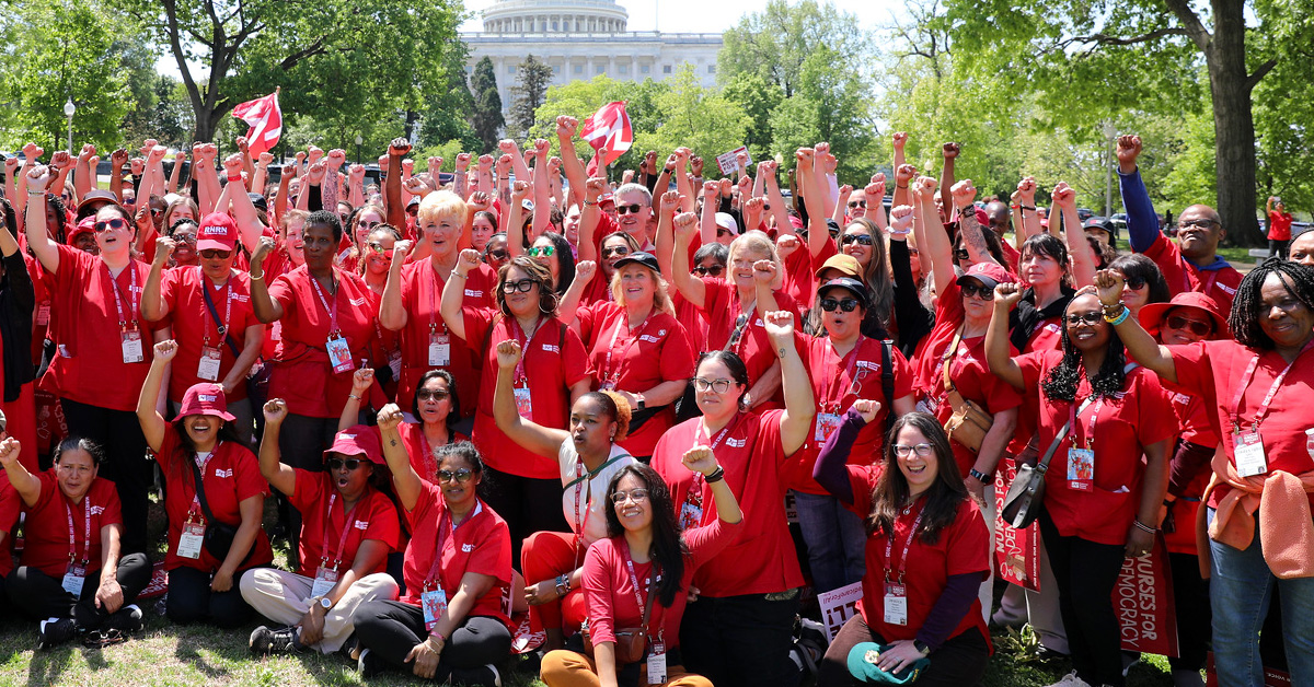 Large group of nurses outside capitol building, smiling, with raised fists