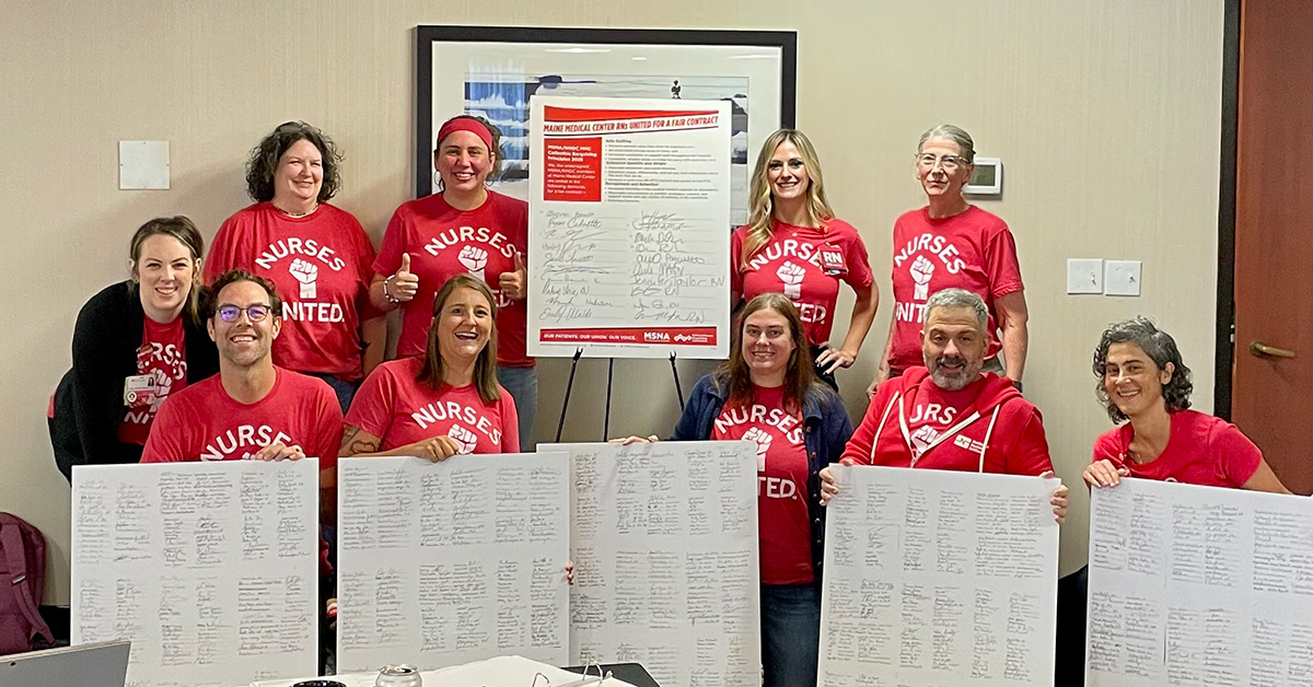 Group of nurses inside, holding large printouts of contract signers