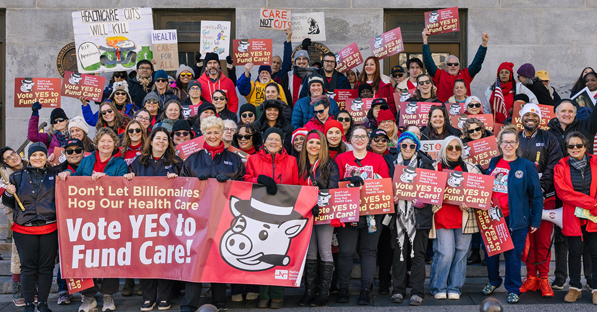 Large group of people holding banner and signs "Don't Let Billionairs Hog Our Health Care: Vote Yes to Fund Care"
