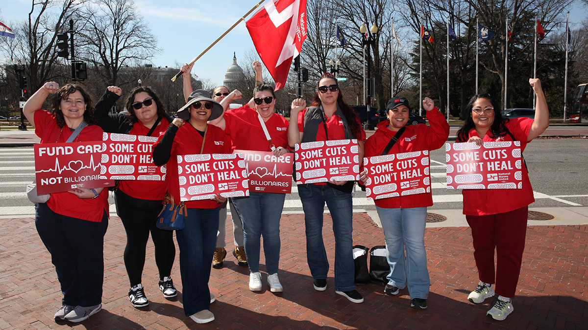 Large group of nurses outside capitol building holding signs "Some Cuts Don't Heal" and "Fund Care Not Billionaires"