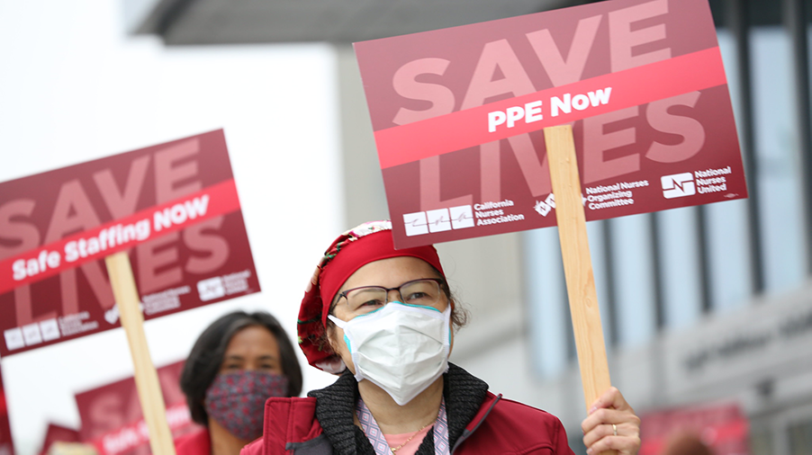 Nurse holds sign "PPE Now"