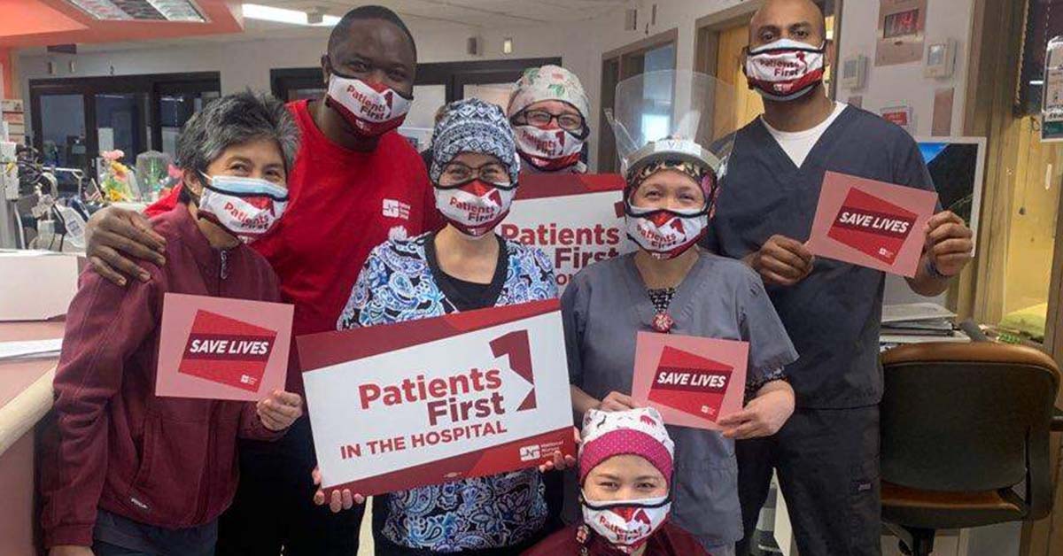 Large group of nurses inside hospital hold signs "Save Lives" and "Patients First"