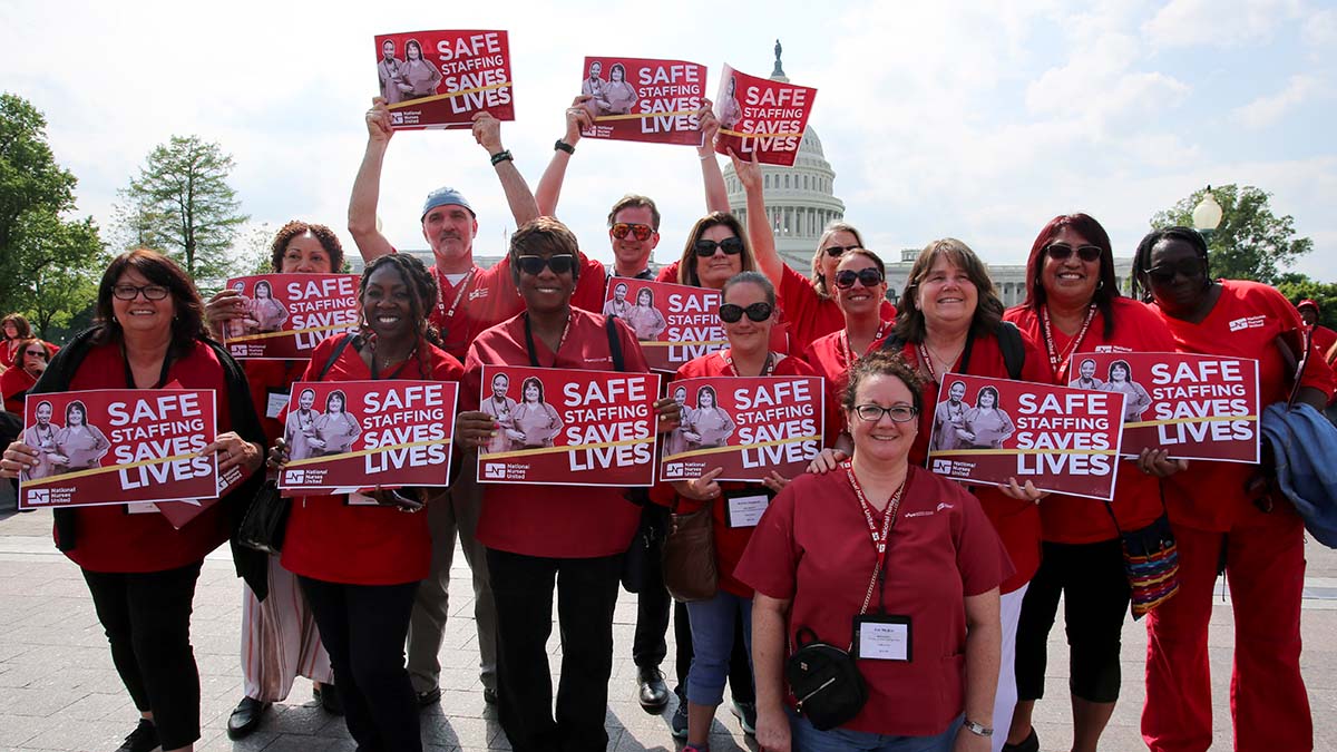 Large group of nurses hold signs "Safe Staffing Saves Lives"