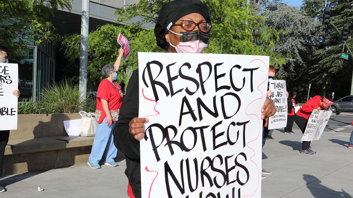 Nurse holds sign "Protect and Respect Nurses Now"
