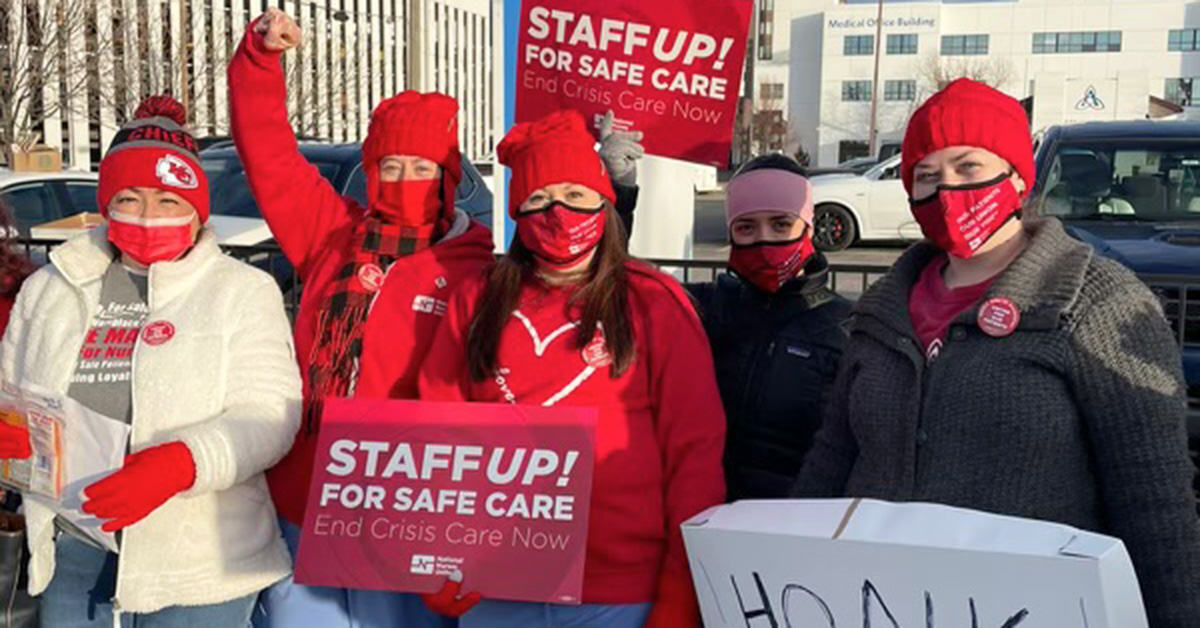 Group of four nurses outside hospital hold signs "Staff up for safe patient care"