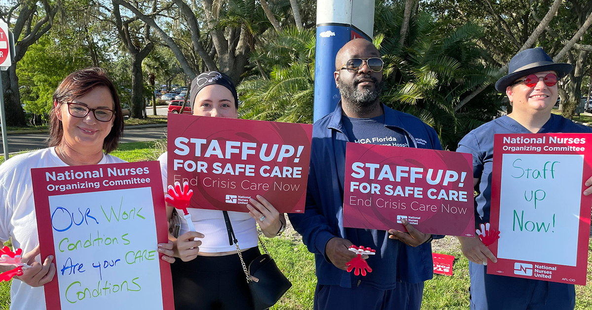 Four nurses outside hold signs "Staff Up for Safe Patient Care"