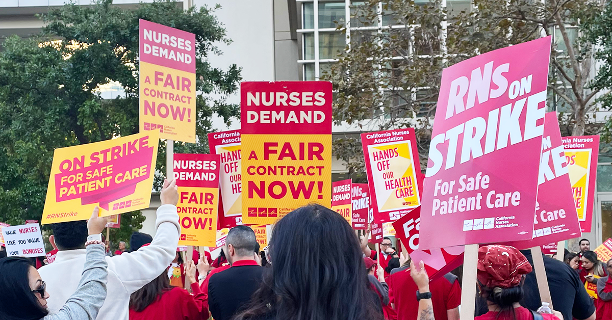 Nurses holding signs "RNs on strike for safe patient care" "Nurses demand a fair contract now!" "Hands off our health care"