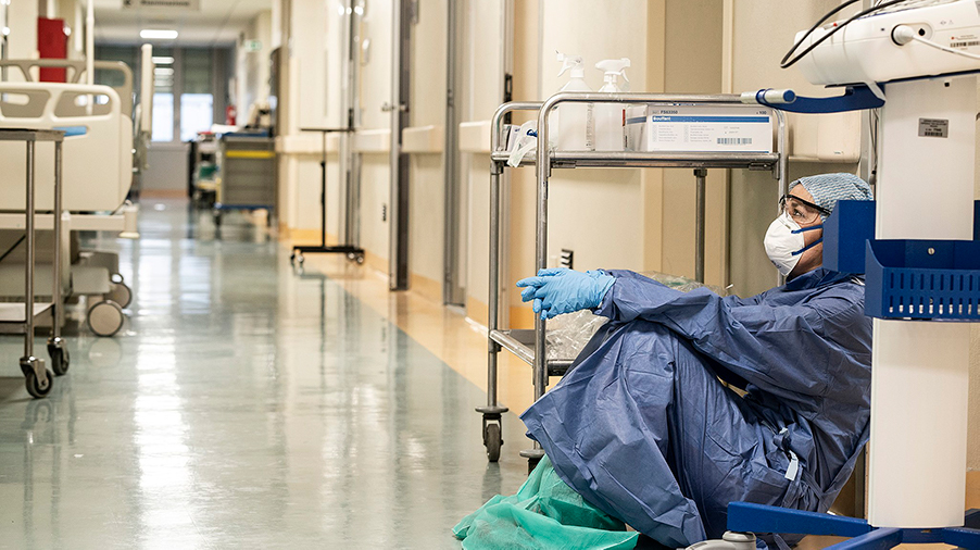 Exhausted nurse sitting on the floor of a hallway with medical equipment.